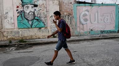 Ein Mann telefoniert während er an einer Wand mit einem Graffiti des verstorbenen kubanischen Führers Fidel Castro läuft.