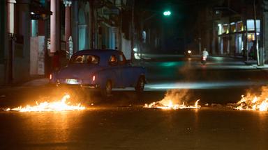 13.05.2026, Kuba, Havanna: Menschen fahren mit einem amerikanischen Oldtimer durch eine Barrikade, die von Anwohnern errichtet wurde, die gegen anhaltende Stromausfälle in Havanna protestieren.