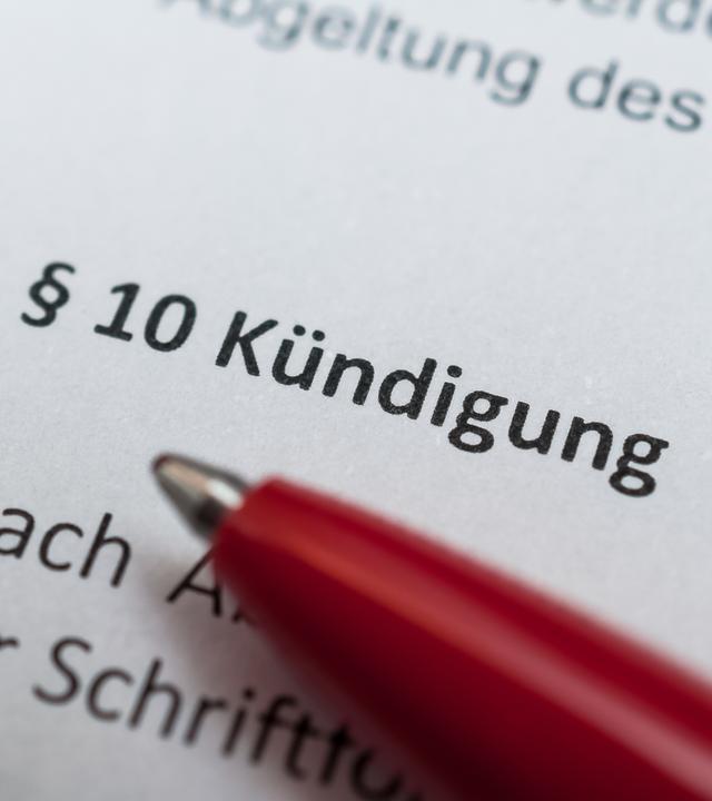 Ein roter Kugelschreiber auf einem Papierdokument. Darauf lesbar "§10 Kündigung"