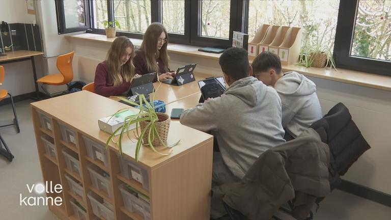 Schülerinnen und Schüler sitzen an Tischen vor Tablets und nutzen künstliche Intelligenz.