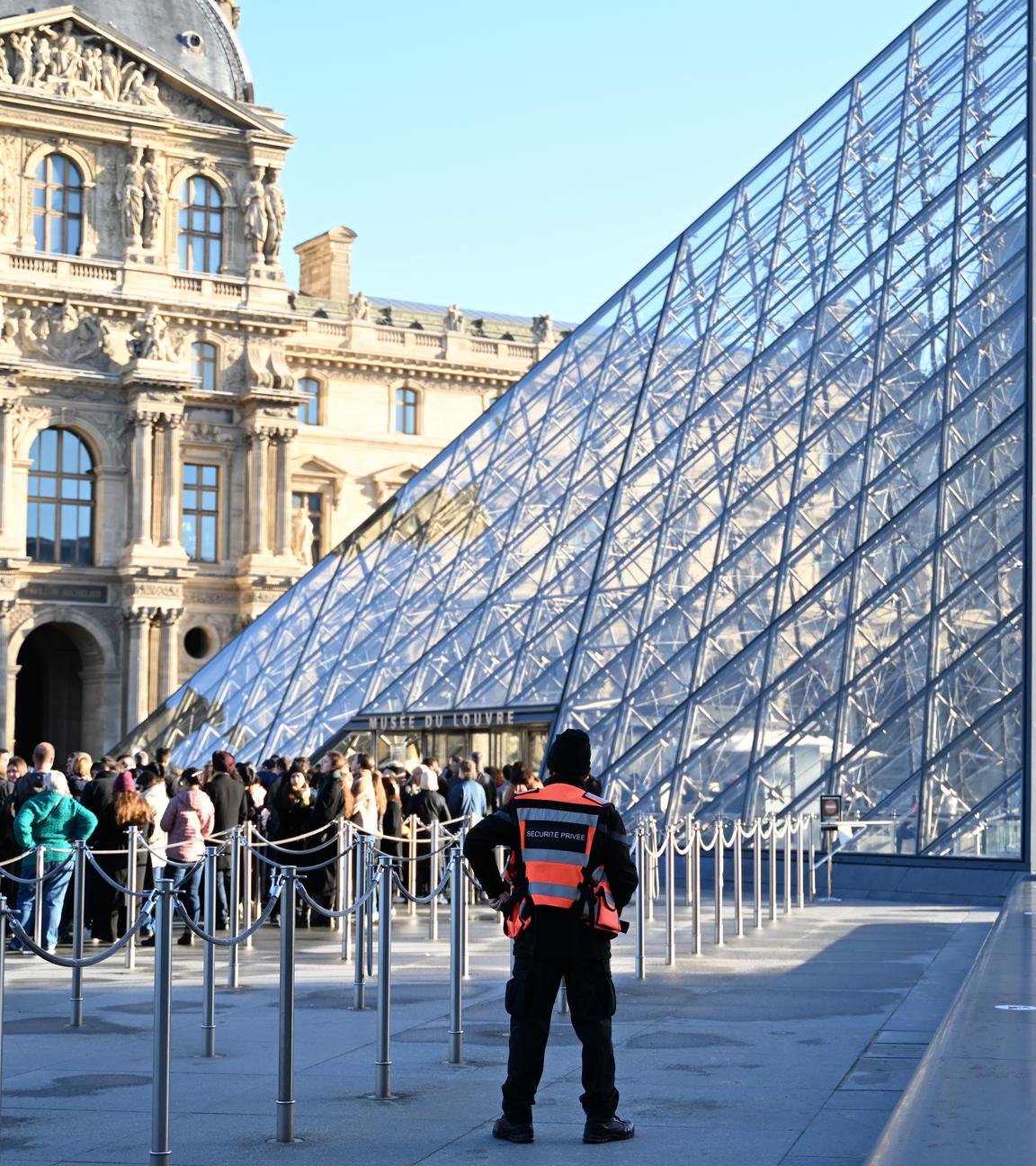 Frankreich, Paris: Vor dem Louvre stehen Menschen Schlange. Ein Sicherheitsbeauftragter beobachtet sie.