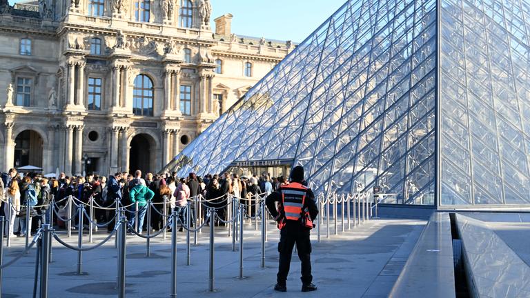 Frankreich, Paris: Vor dem Louvre stehen Menschen Schlange. Ein Sicherheitsbeauftragter beobachtet sie.
