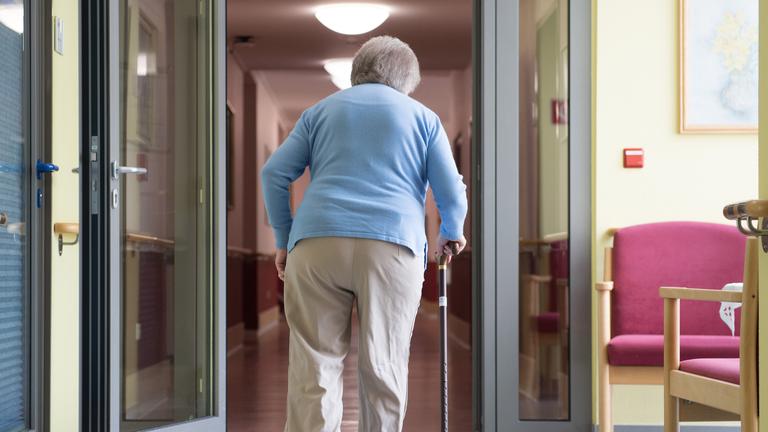 Eine ältere Frau mit einem gekrümmten Rücken geht an einem Gehstock.