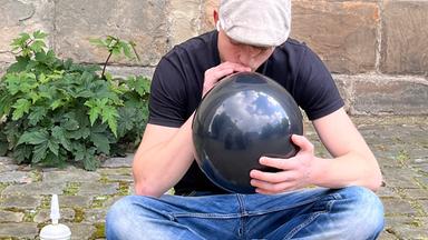 Ein Jugendlicher sitzt im Freien und zieht das Lachgas aus einem Ballon heraus.