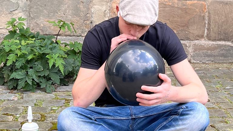 Ein Jugendlicher sitzt im Freien und zieht das Lachgas aus einem Ballon heraus.