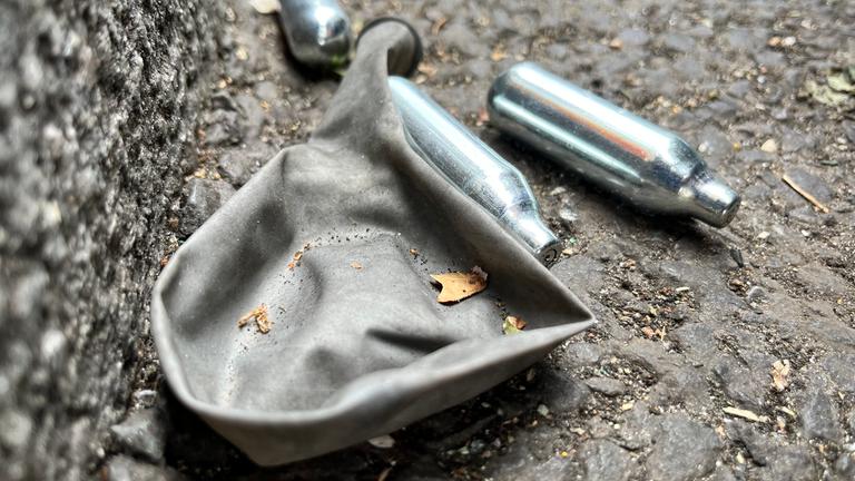 Leere Lachgas-Patronen und ein Luftballon auf dem Boden.