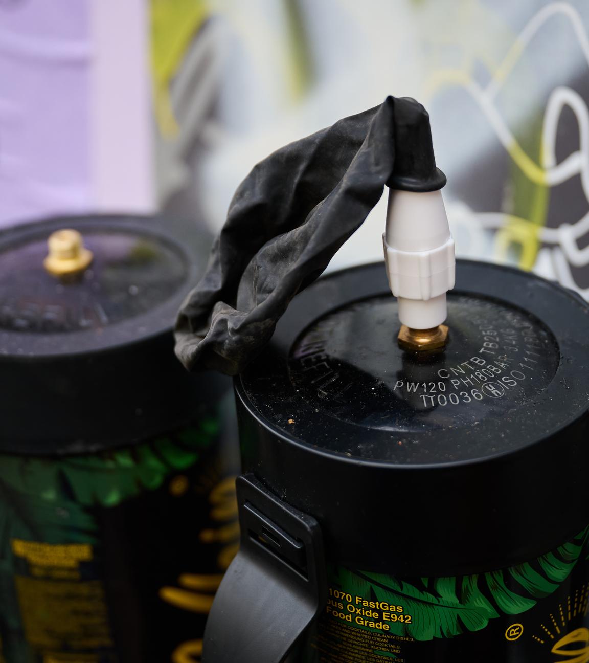 12.11.2025, Berlin: Zwei benutzte Lachgasflaschen und ein benutzter Luftballon befinden sich auf einer Fensterbank vor einem Spätkauf.