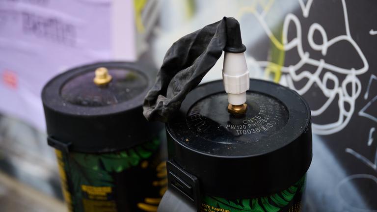 12.11.2025, Berlin: Zwei benutzte Lachgasflaschen und ein benutzter Luftballon befinden sich auf einer Fensterbank vor einem Spätkauf.