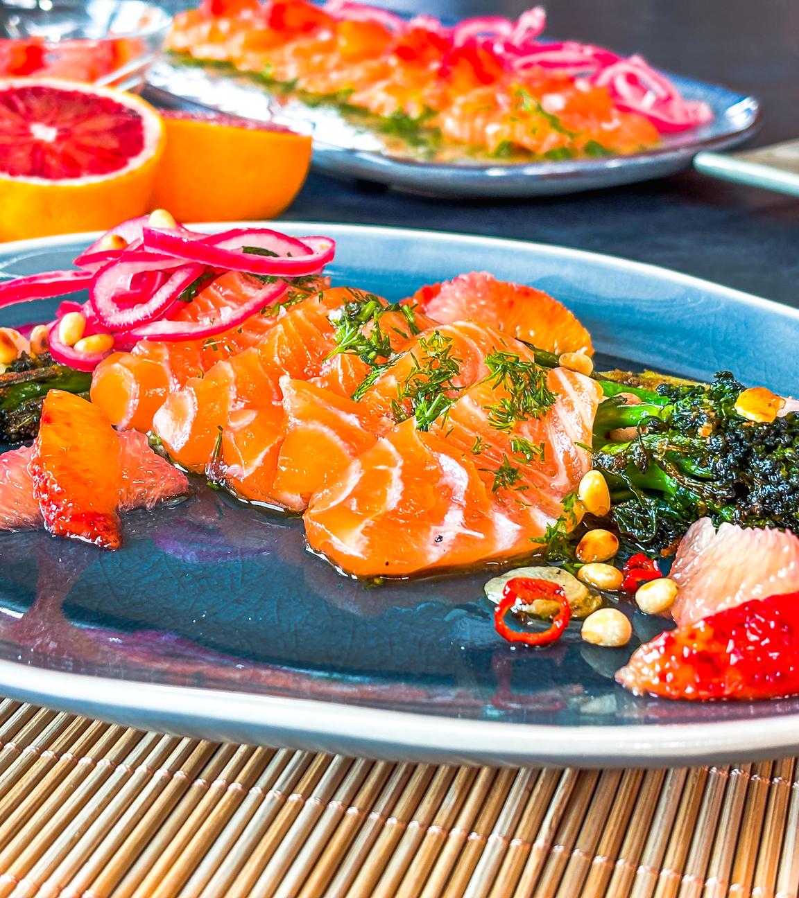 Lachs Crudo mit Grapefruit auf einem blauen Teller serviert.