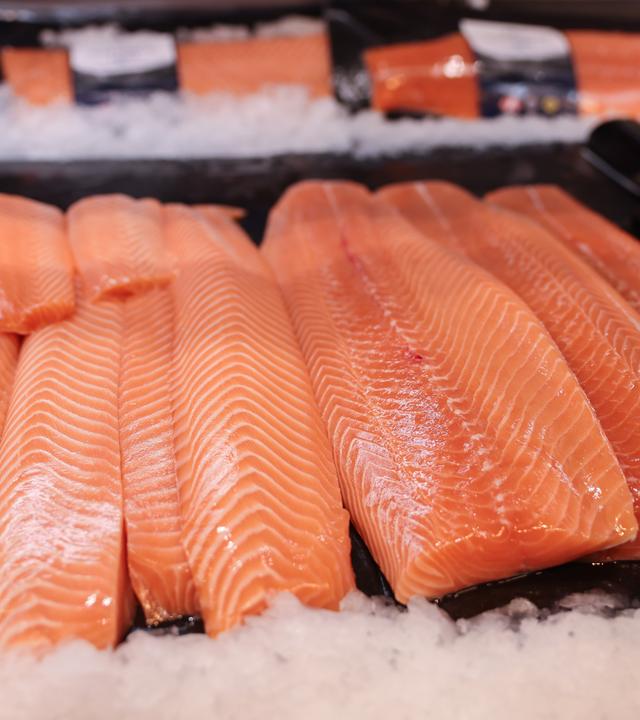 Lachs in verschiedenen Qualitäten und Zuschnitten liegt in der Auslage einer Fischtheke.