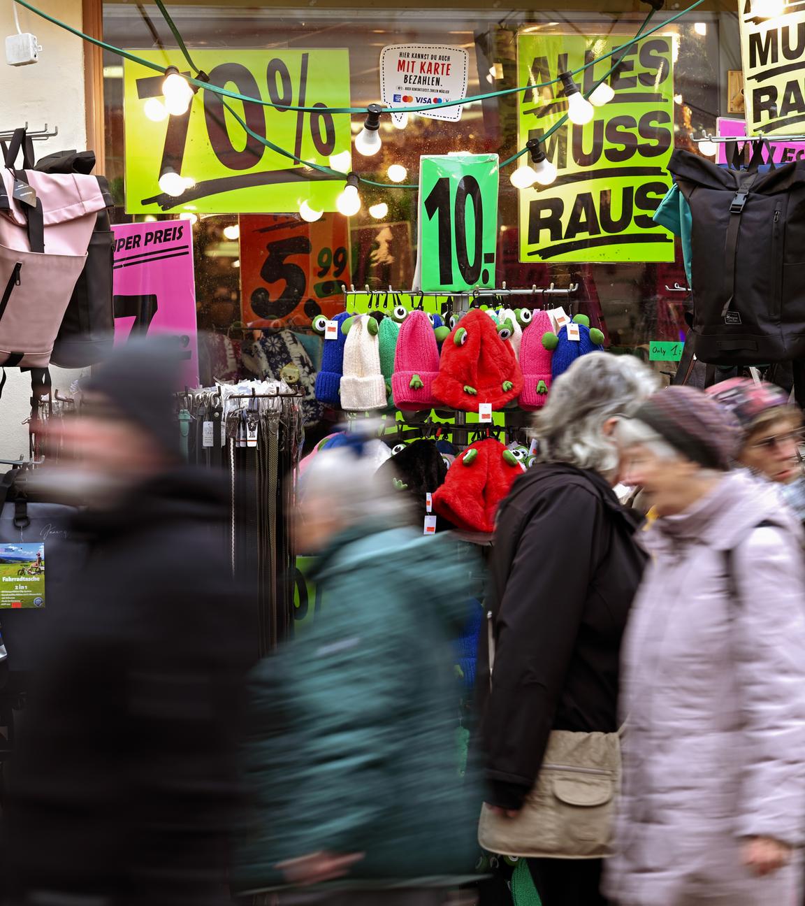 Passanten gehen an einem Geschäft mit vielen Plakaten vorbei, auf denen der Ausverkauf und Rabatte angekündigt werden.