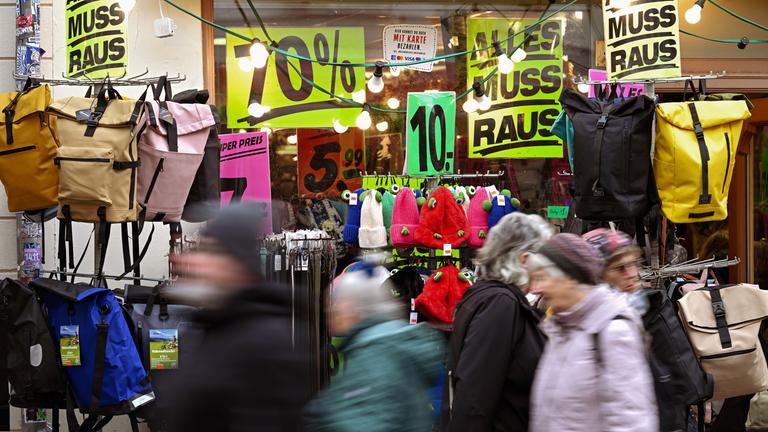 Passanten gehen an einem Geschäft mit vielen Plakaten vorbei, auf denen der Ausverkauf und Rabatte angekündigt werden.
