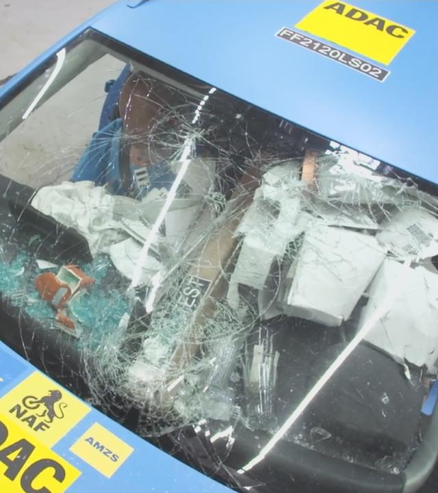 Auto mit kaputter Frontscheibe, wo man verschiedene lose Gepäckstücke unordentlich verteilt im Auto von oben sieht.