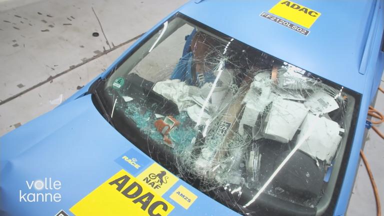 Auto mit kaputter Frontscheibe, wo man verschiedene lose Gepäckstücke unordentlich verteilt im Auto von oben sieht.