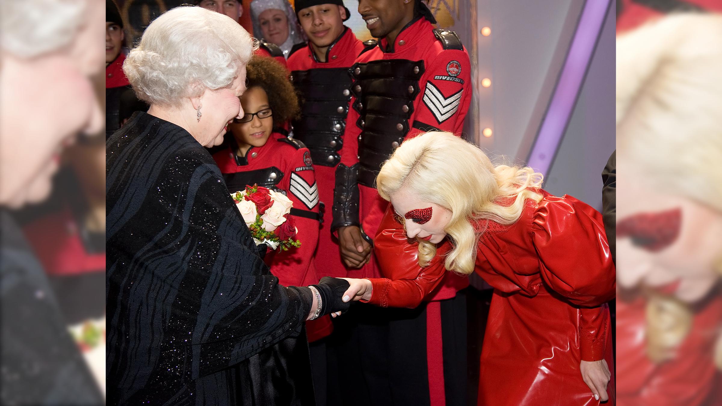 Lady Gaga knickst 2009 vor Queen Elisabeth. Sie trägt ein rotes Lackkleid.