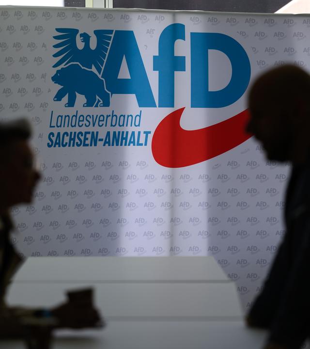 Landesparteitag der AfD Sachsen-Anhalt im April 2026: Zwei Teilnehmende stehen vor dem Parteilogo