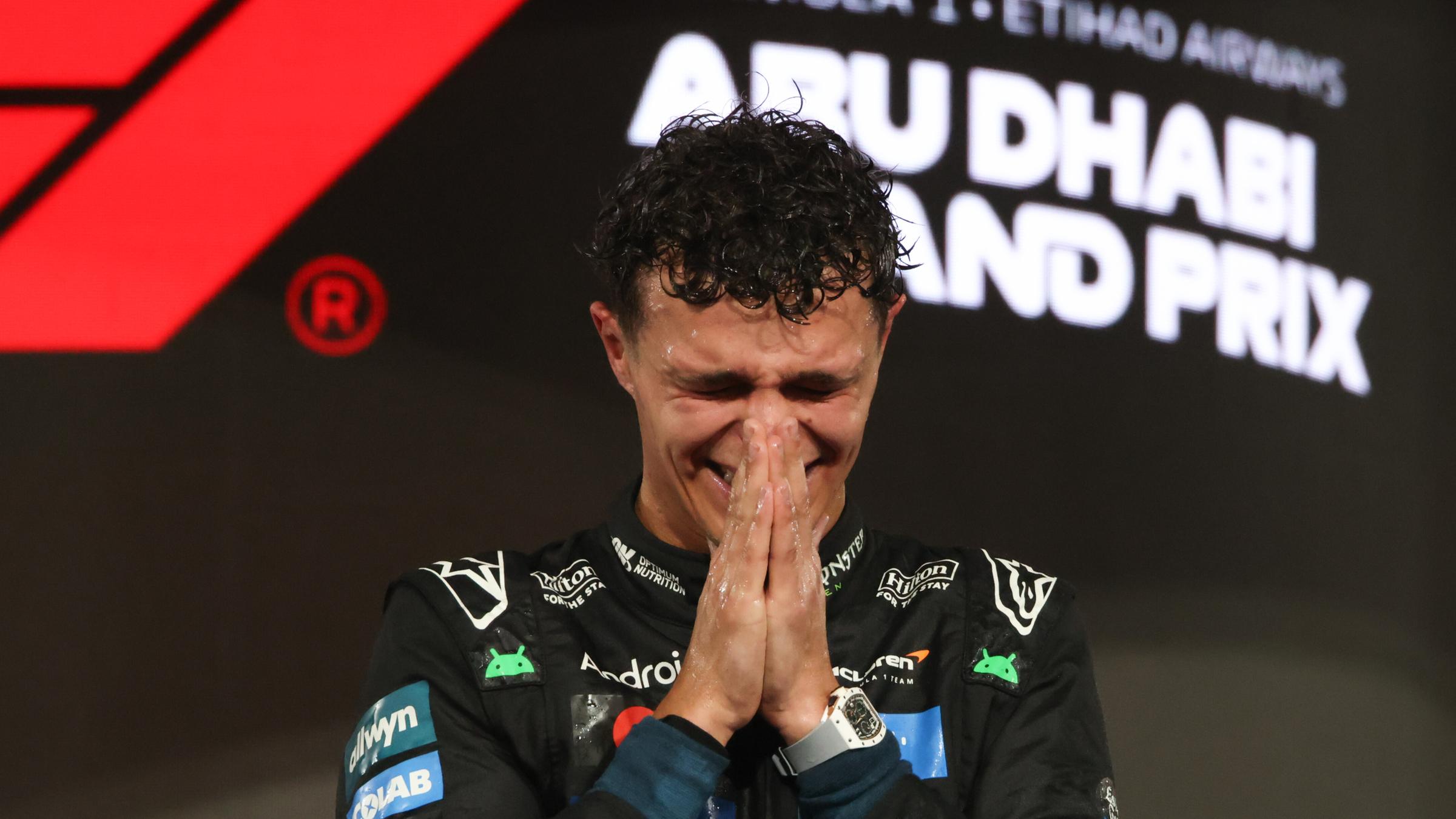 Der neue Formel-Weltmeister Lando Norris faltet bei der Siegerehrung in Abu Dhabi die Hände vorm Gesicht.