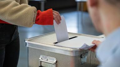 Eine Frau steckt ihren Stimmzettel für die Bundestagswahl in einem Wahllokal in eine Wahlurne.