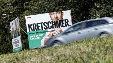Ein graues Auto fährt an einem großen Wahlkampfplakat von Michael Kretschmer (CDU) vorbei.