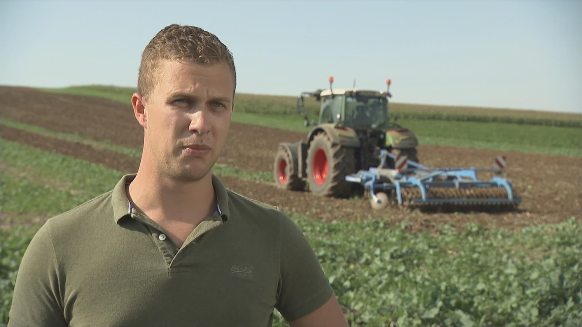 Auf dem Bild sieht man einen Landwirt und im Hintergrund ein Traktor.