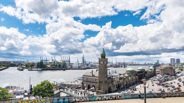 Wolken sind über den Landungsbrücken und dem Hamburger Hafen zu sehen.