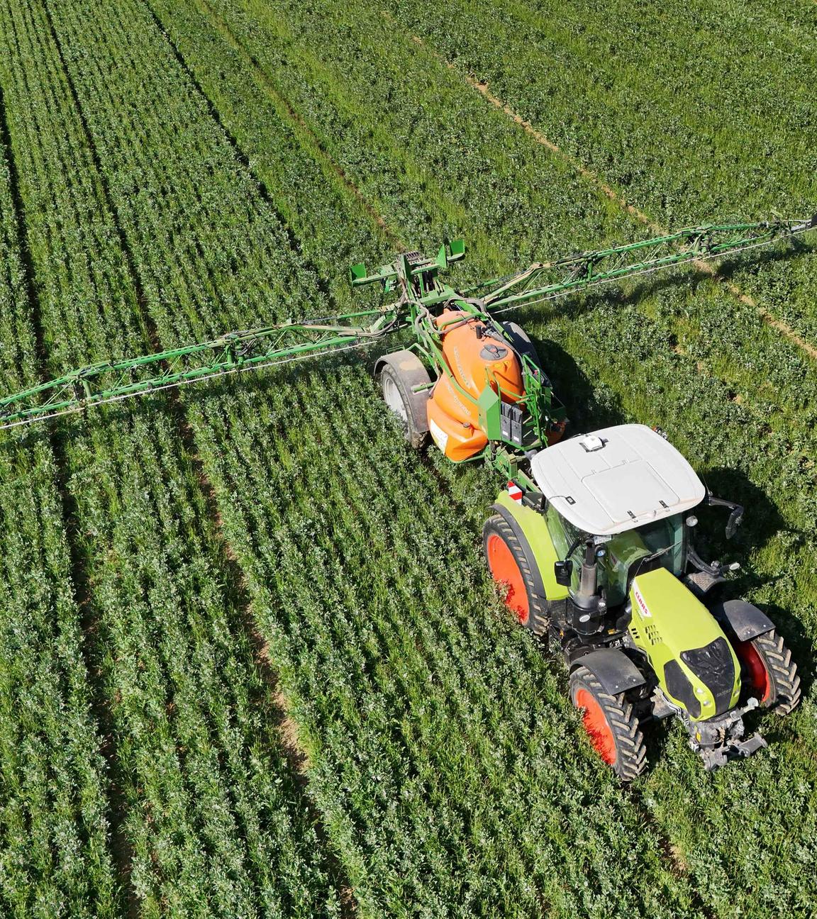 Symbolbild: Ein Landwirt fährt mit seinem Traktor ueber ein  grünes Feld und düngt