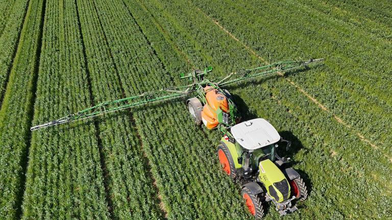 Symbolbild: Ein Landwirt fährt mit seinem Traktor ueber ein  grünes Feld und düngt