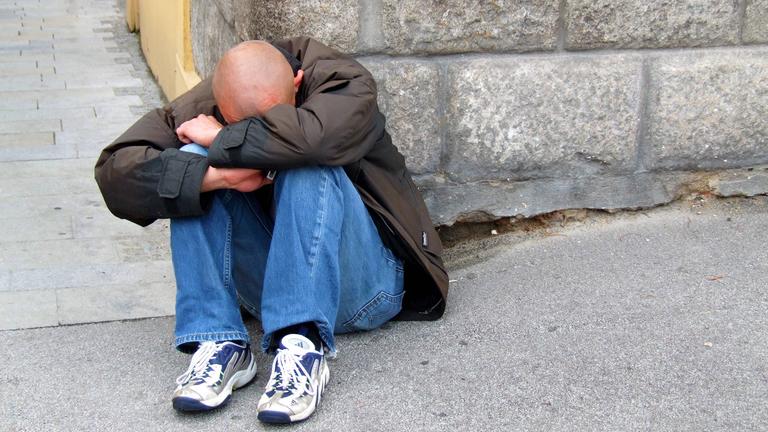 Mann sitzt verzweifelt auf Bordstein