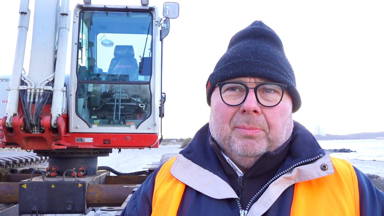 Lars Hoppe von der Firma MBN steht am 25.03.2026 in der Nähe von einem gestrandeten Wal in der Ostsee am Timmendorfer Strand an einem Bagger. 