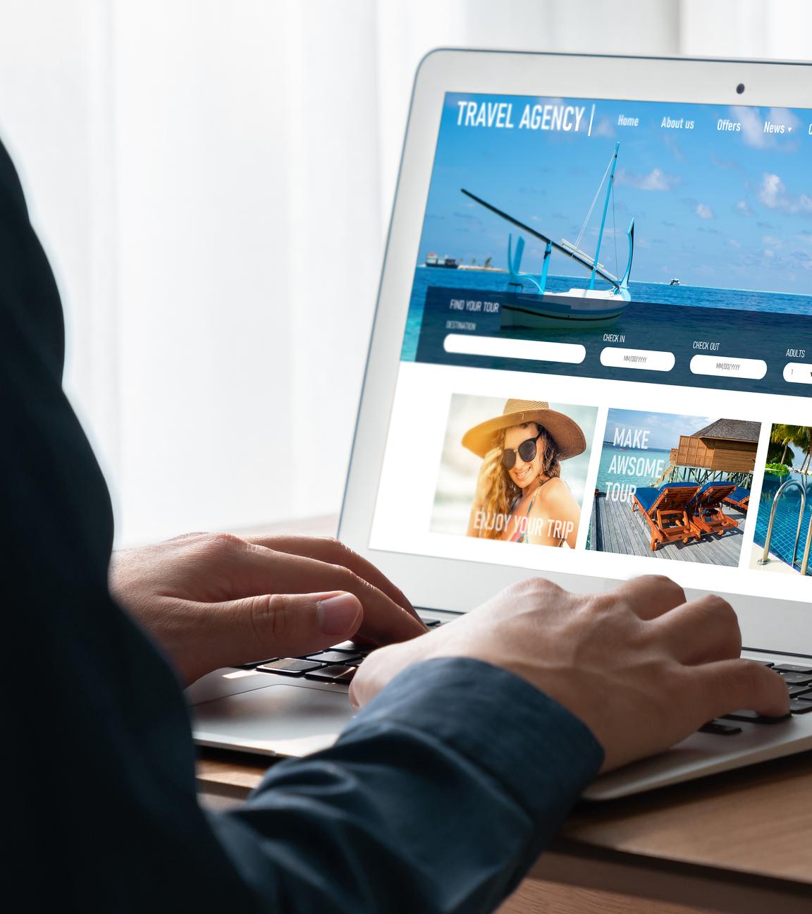 Eine Person sitzt vor einem aufgeklappten Laptop und schaut sich Angebote auf einer Reise-Website an. 