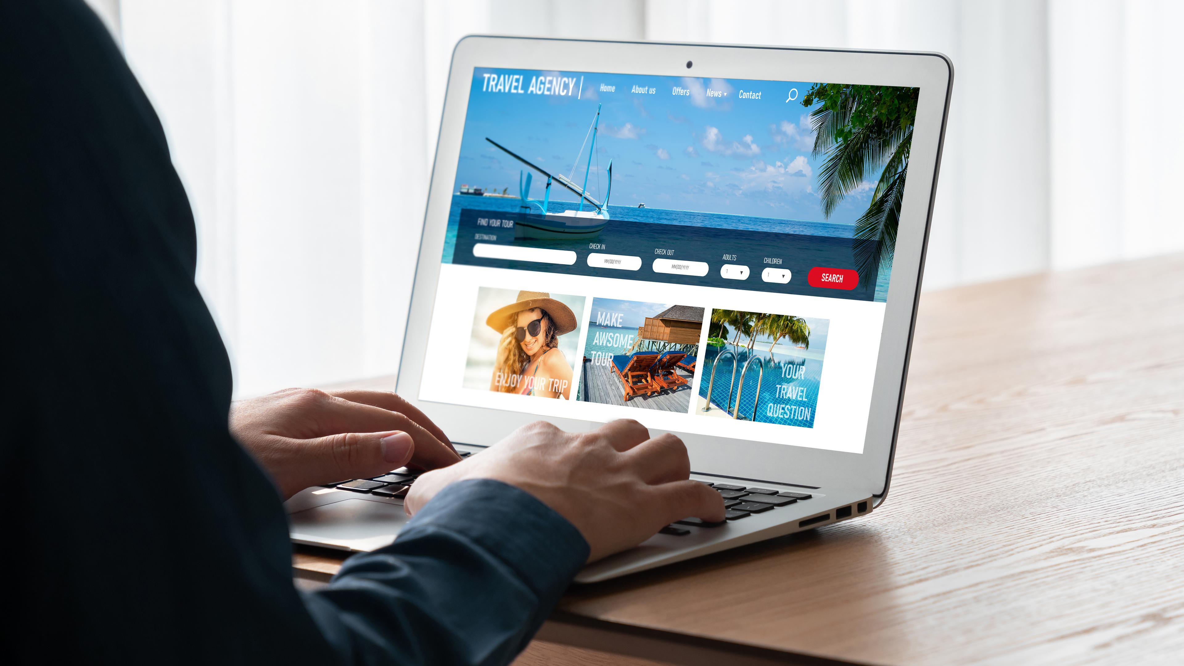 Eine Person sitzt vor einem aufgeklappten Laptop und schaut sich Angebote auf einer Reise-Website an. 