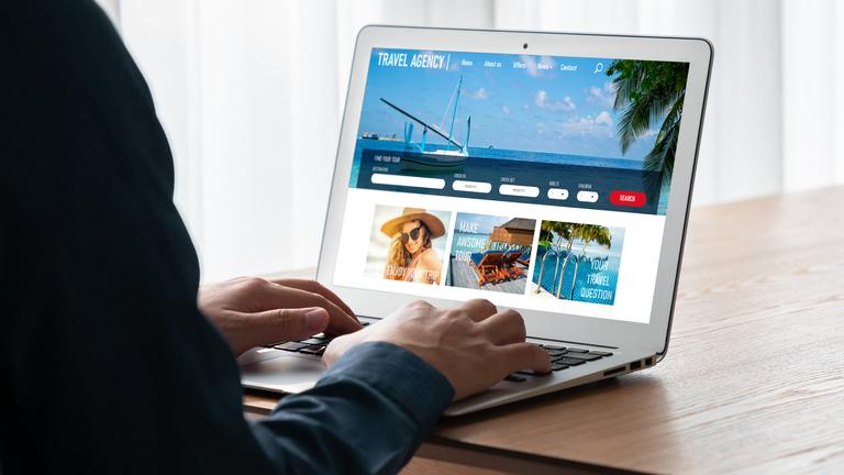 Eine Person sitzt vor einem aufgeklappten Laptop und schaut sich Angebote auf einer Reise-Website an. 