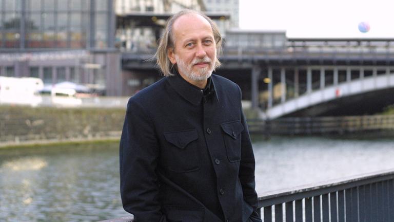 Der Autor László Krasznahorkai steht vor der Spree in Berlin 