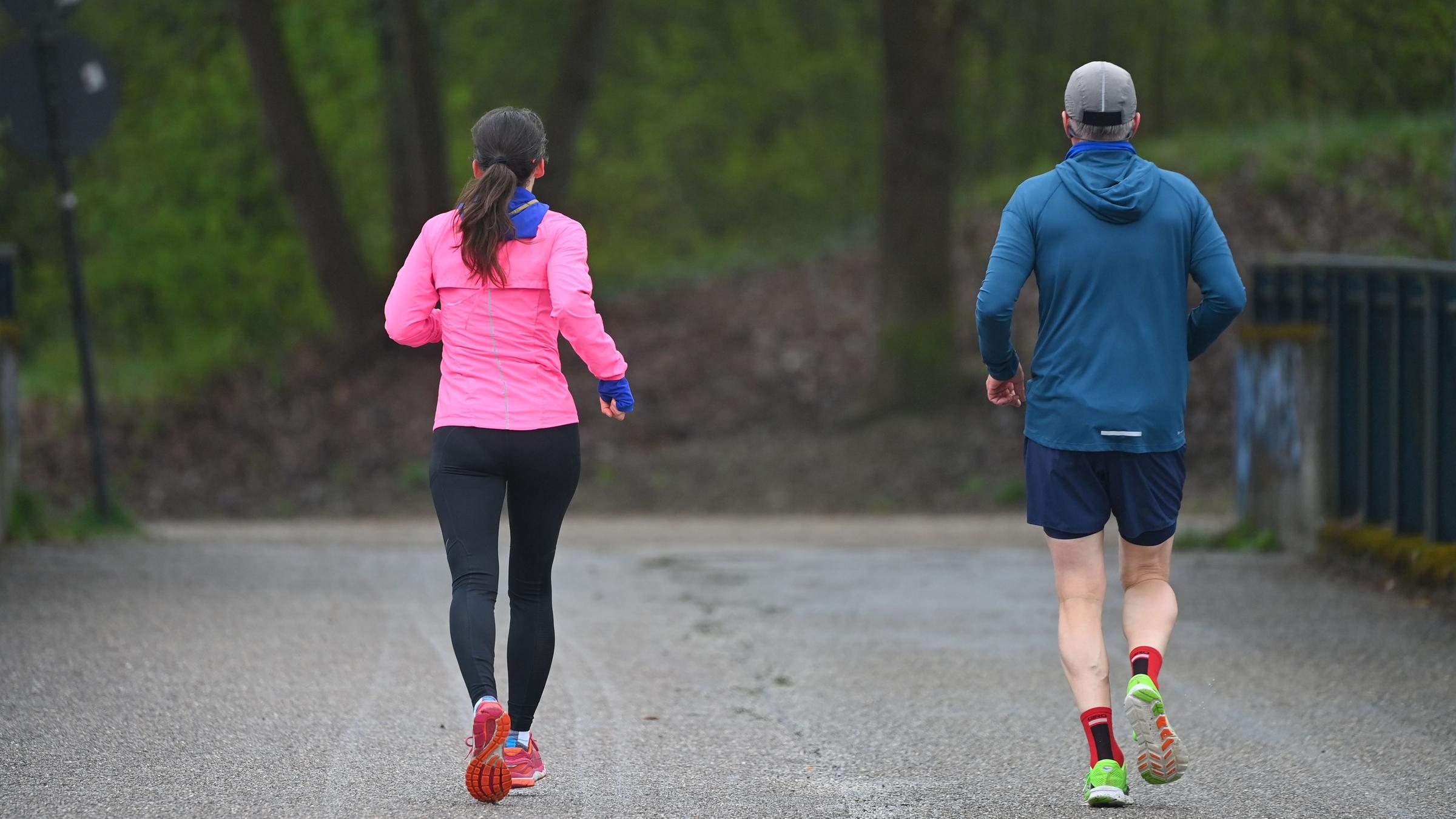 Zwei Personen joggen durch einen Park.