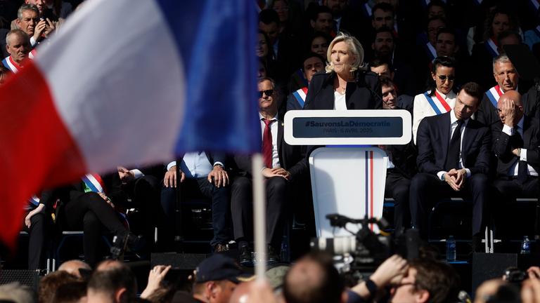 Marine Le Pen steht an einem Rednerpult, im Vordergrund weht eine französische Flagge.
