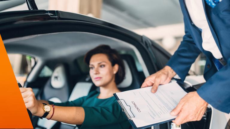 Frau sitzt im Auto, im Hintergrund ein Verkäufer