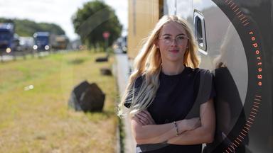 Melina steht neben ihrem Lkw, im Hintergrund befindet sich die volle Autobahn. Sie schaut freundlich in die Kamera.