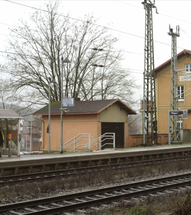 Zu sehen ist ein Bahnhof in einem Dorf.