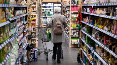Eine Frau geht mit ihrem Einkaufswagen durch einen Supermarkt.