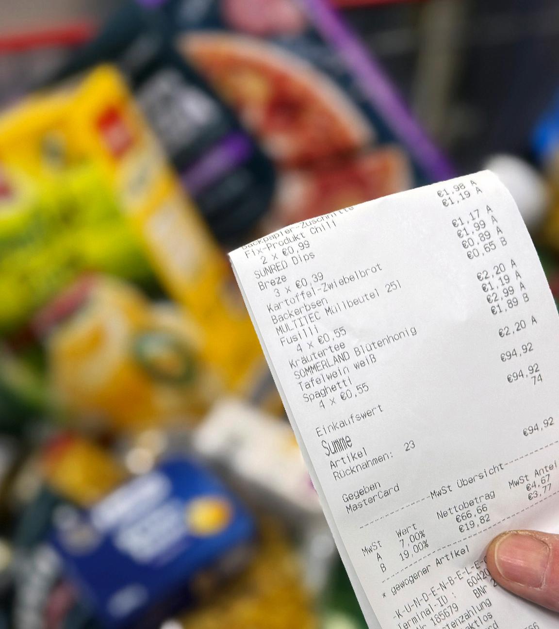 Hand hält Kassenbon über gefülltem Einkaufswagen