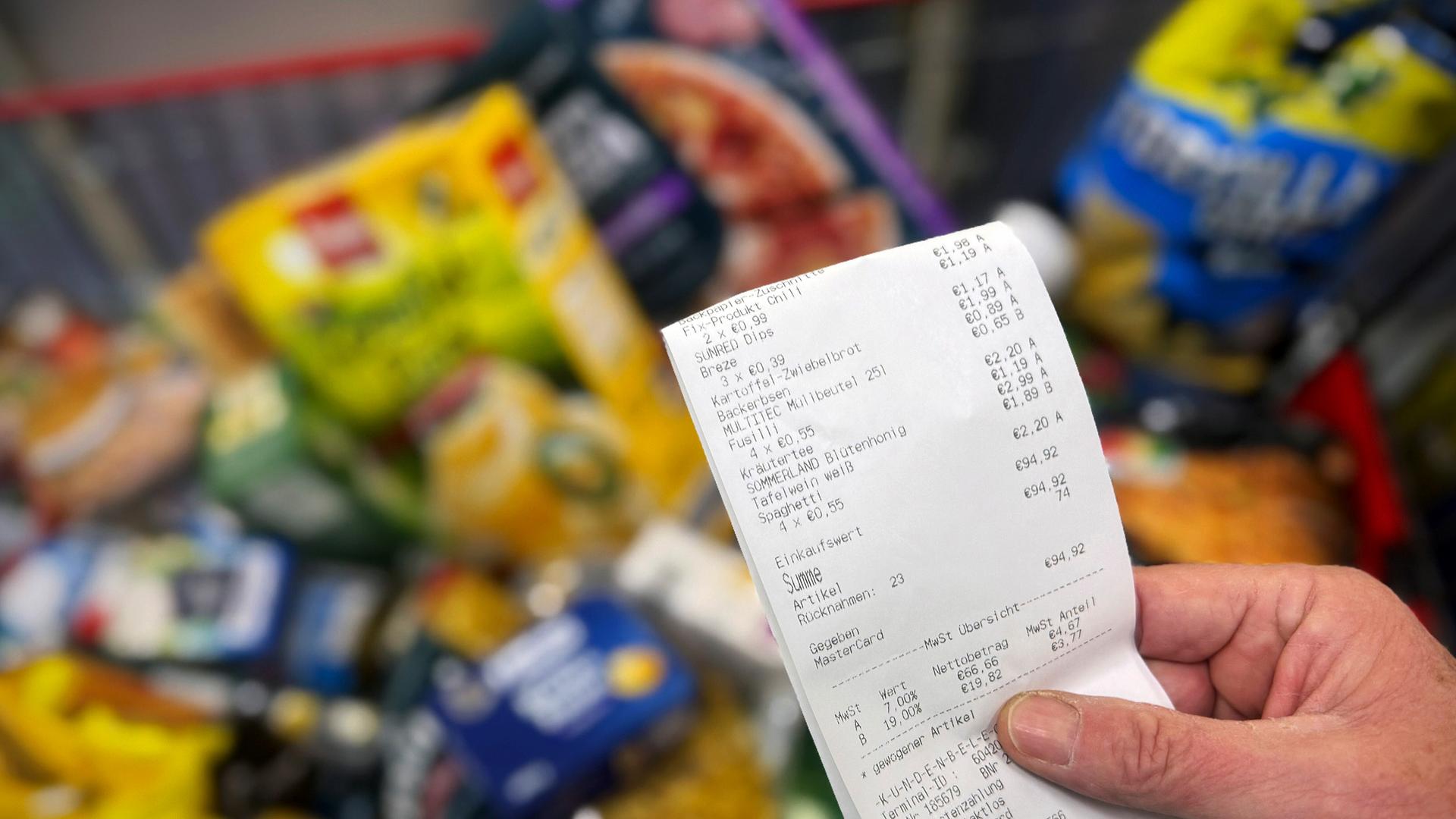 Hand hält Kassenbon über gefülltem Einkaufswagen