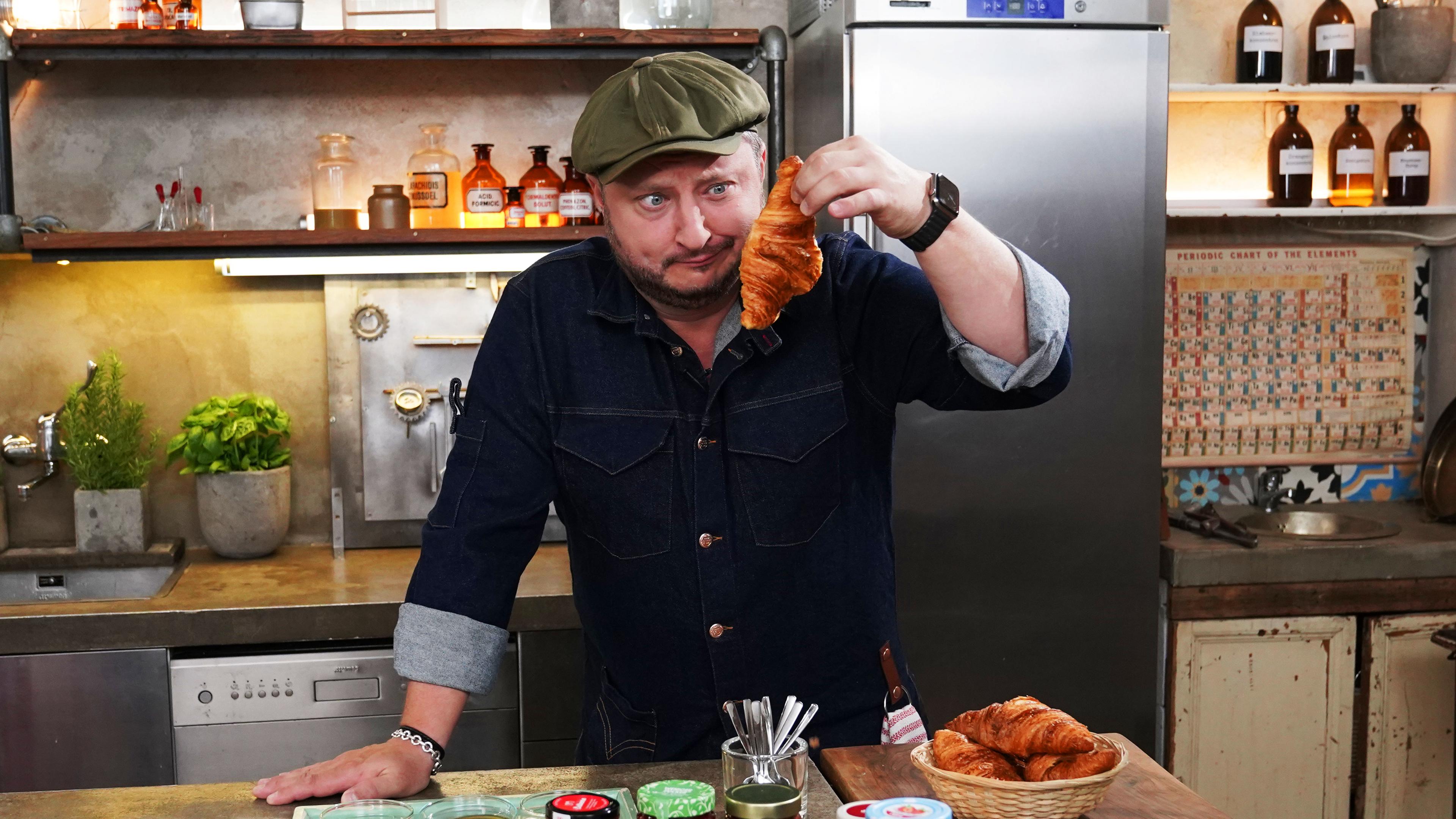 Sebastian Lege hat zuckerreduzierten Fruchtaufstrich eingekauft und wirft einen kritischen Blick auf ein Croissant.