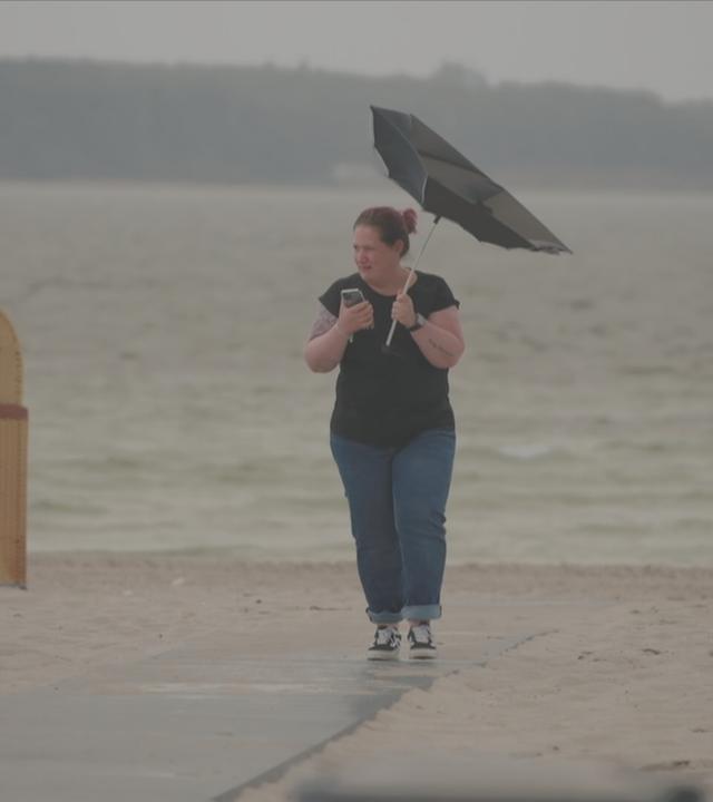 Frau mit Regenschirm am Strand