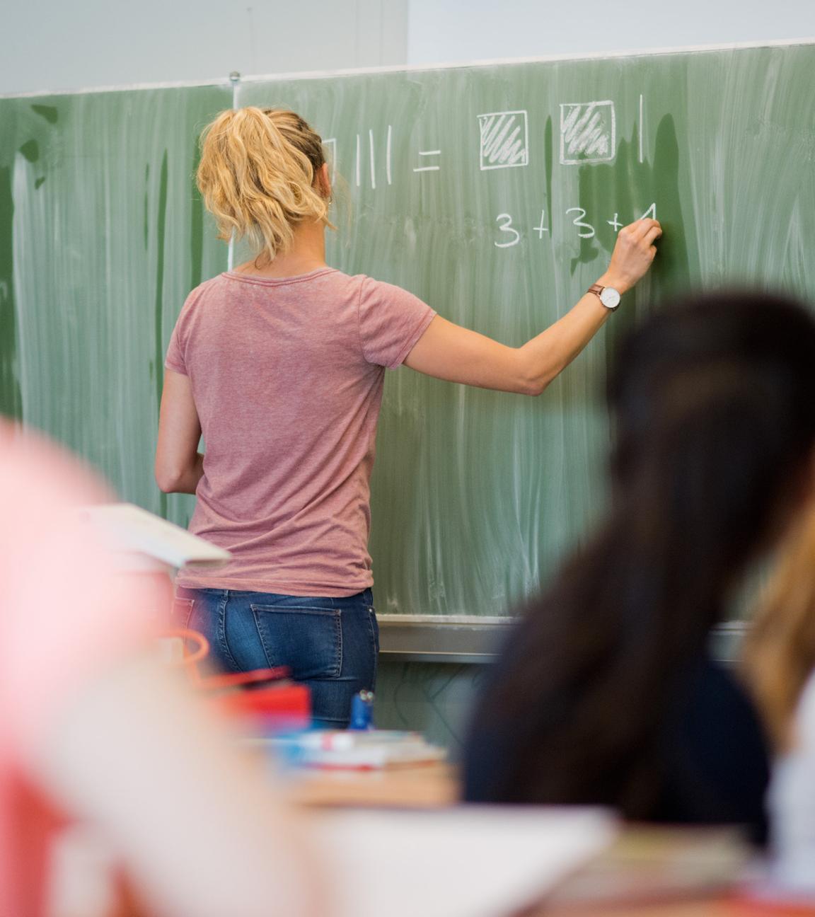 Eine junge lehrerin schreibt an eine schultafel im mathematikunterricht.