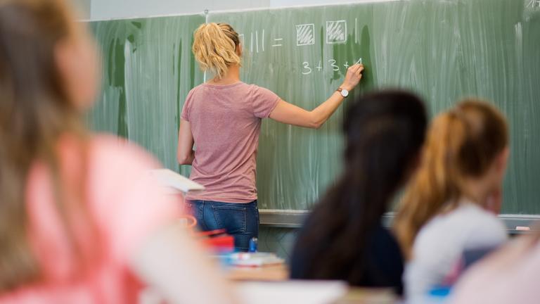Eine junge lehrerin schreibt an eine schultafel im mathematikunterricht.