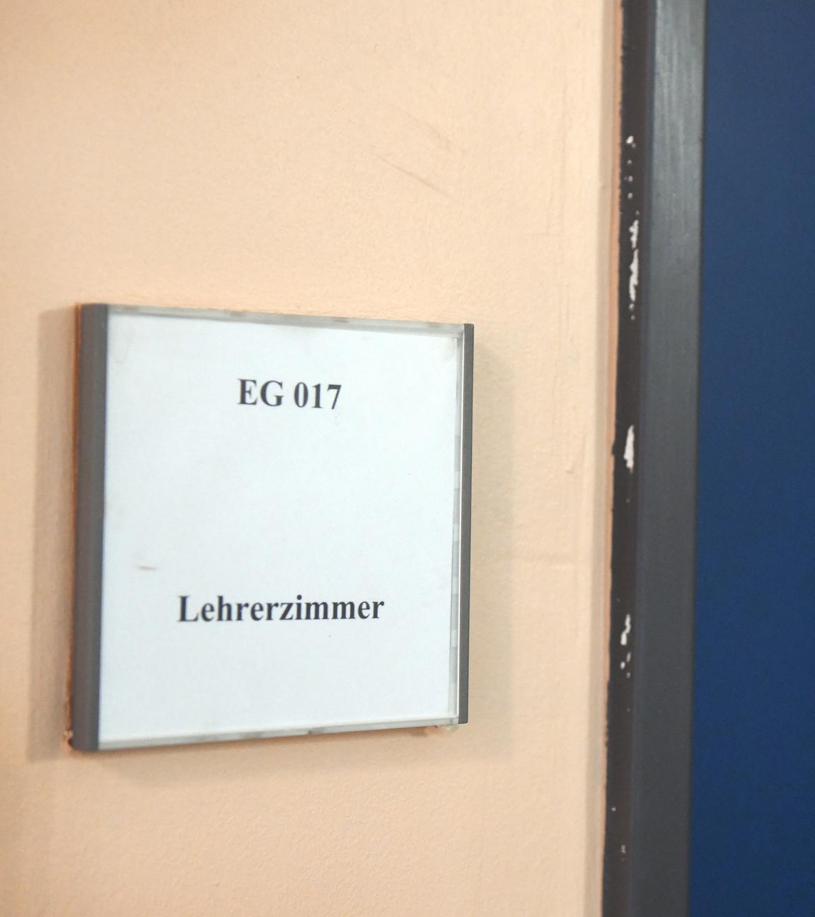 Ein Mann geht an einem Schild vorbei, das den Weg zum Lehrerzimmer weist. 