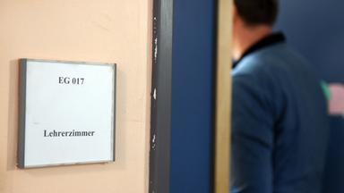 Ein Mann geht an einem Schild vorbei, das den Weg zum Lehrerzimmer weist. 