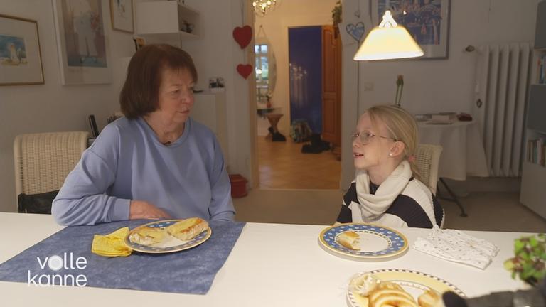 Ältere Frau und Mädchen sitzen bei Kuchen am Tisch und sprechen miteinander