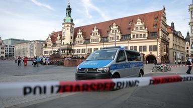 Leipzig: Ein Polizeiwagen parkt hinter einer Polizeiabsperrung an der Stelle, wo ein Auto in eine Menschengruppe gefahren ist
