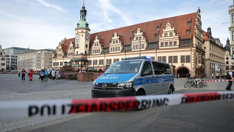 Leipzig: Ein Polizeiwagen parkt hinter einer Polizeiabsperrung an der Stelle, wo ein Auto in eine Menschengruppe gefahren ist
